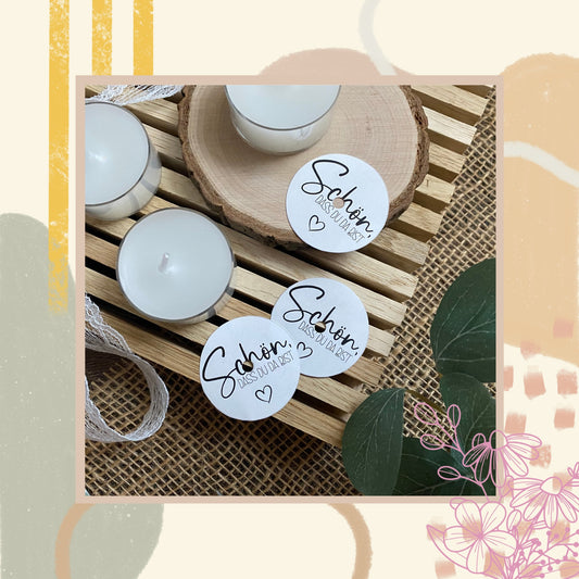 DIY-Tischdekoration mit Teelichtern, die mit runden „Schön, dass du da bist“-Stickern beklebt sind, präsentiert auf einer rustikalen Holzscheibe mit Eukalyptus.