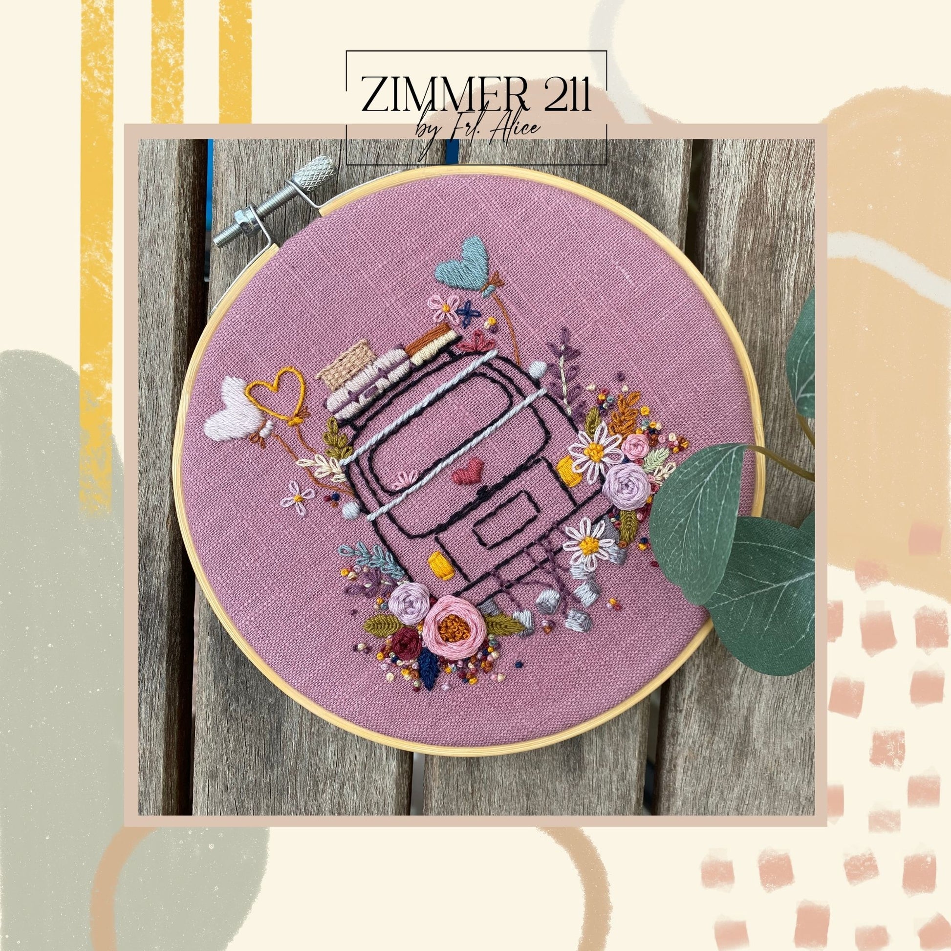 Zimmer211 Stickvorlage: Ein gestickter Vintage-Bus auf altrosa Leinenstoff, verziert mit bunten Blumen in Rosa- und Gelbtönen sowie Herz-Ballons, präsentiert in einem hölzernen Stickrahmen auf rustikalem Holzgrund.